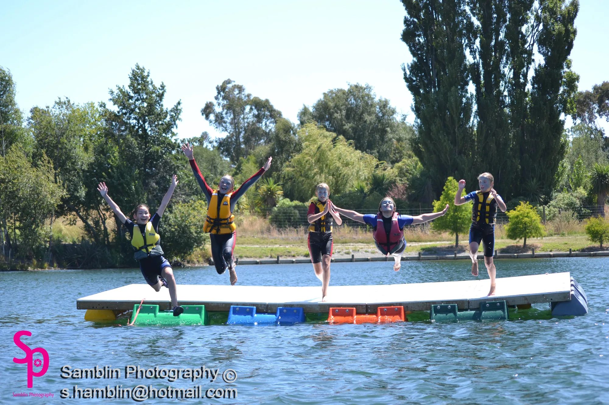 Kids in life jackets jumping off a swim platform on coloured pods