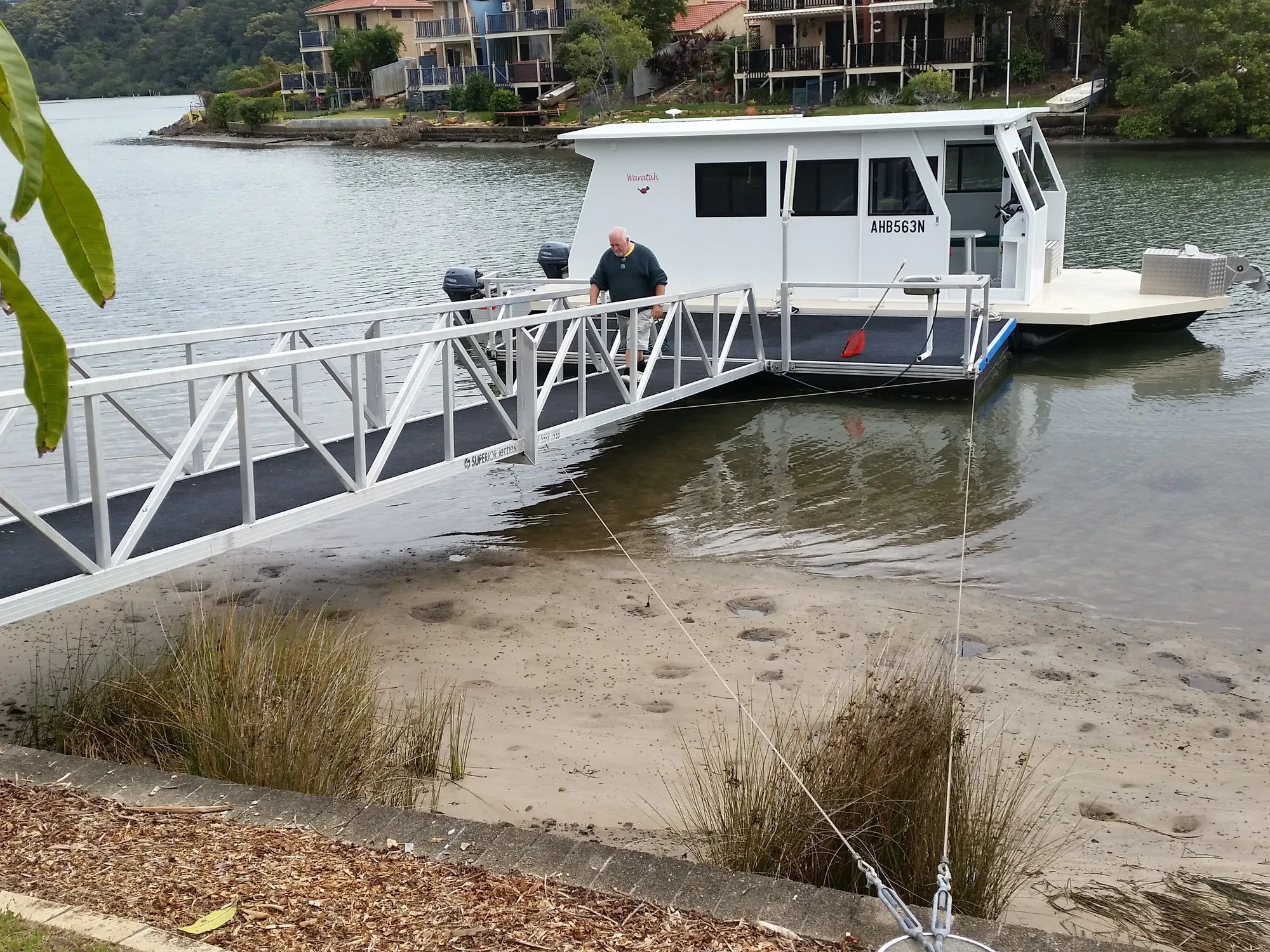 Enclosed white houseboat moored at the end of an aluminium gangway