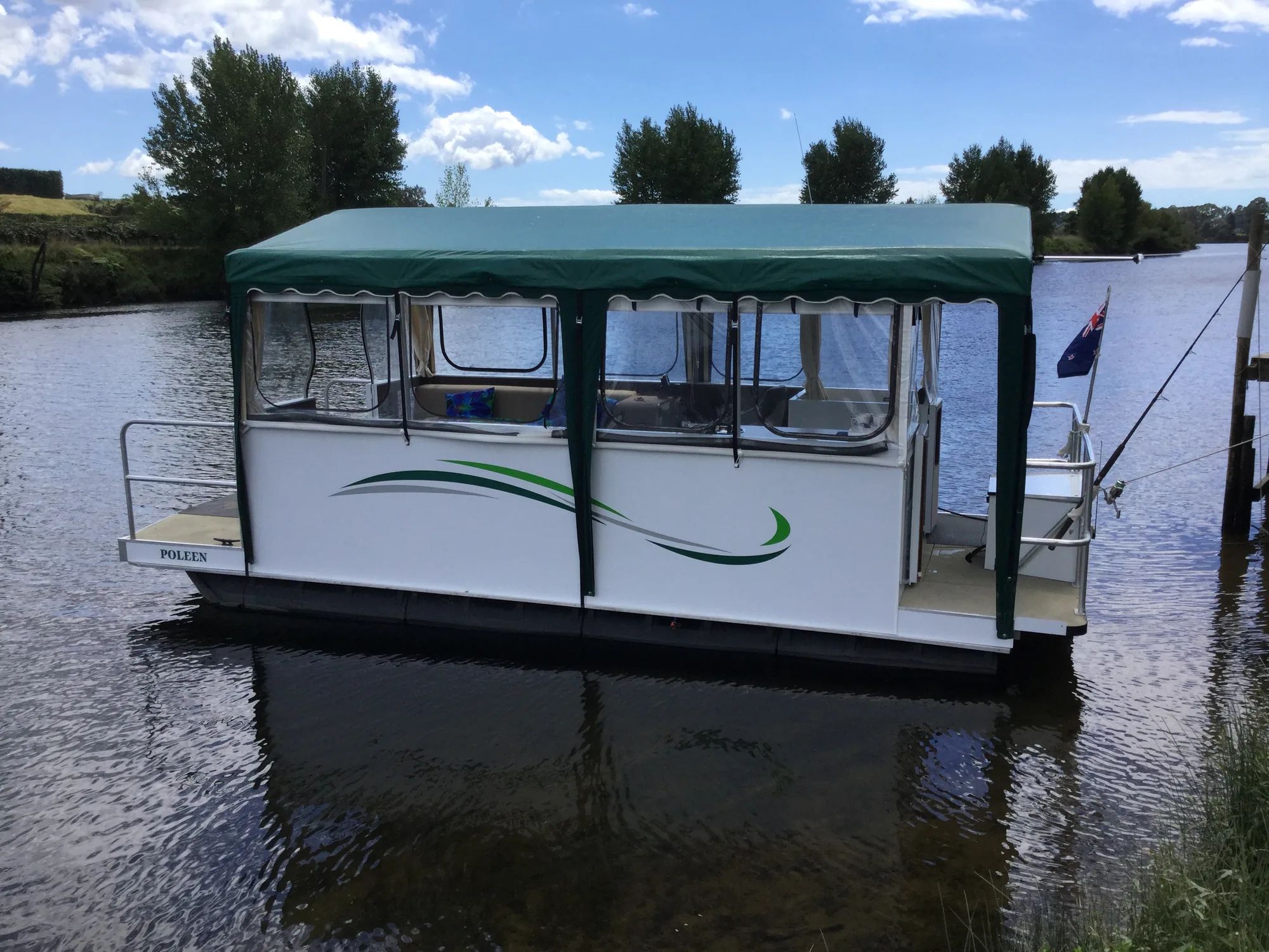 Houseboat with a green canopy and clear side curtains moored on a river