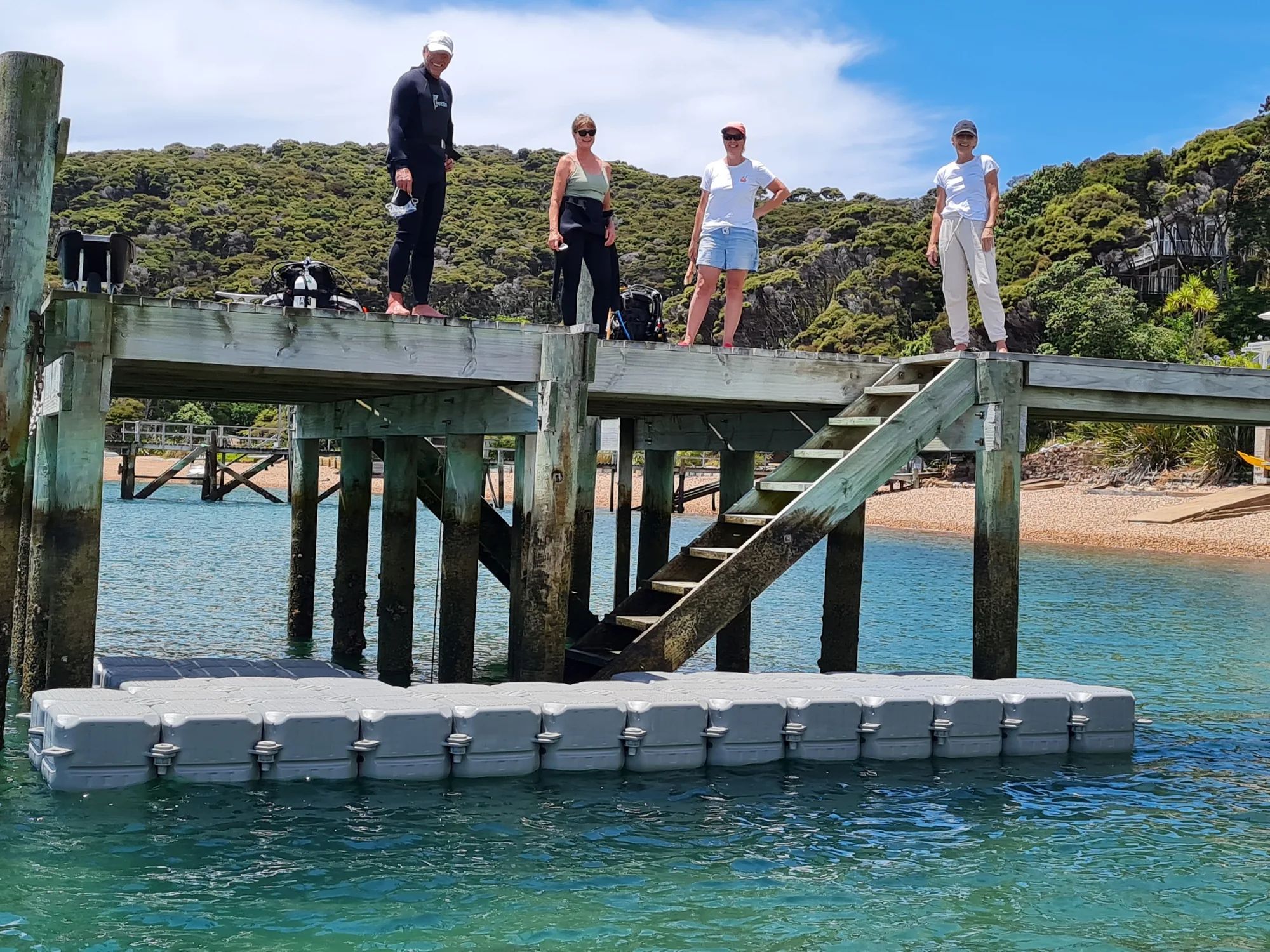Modular floating dock under a public wharf in the Bay of Islands, with people on the wharf above