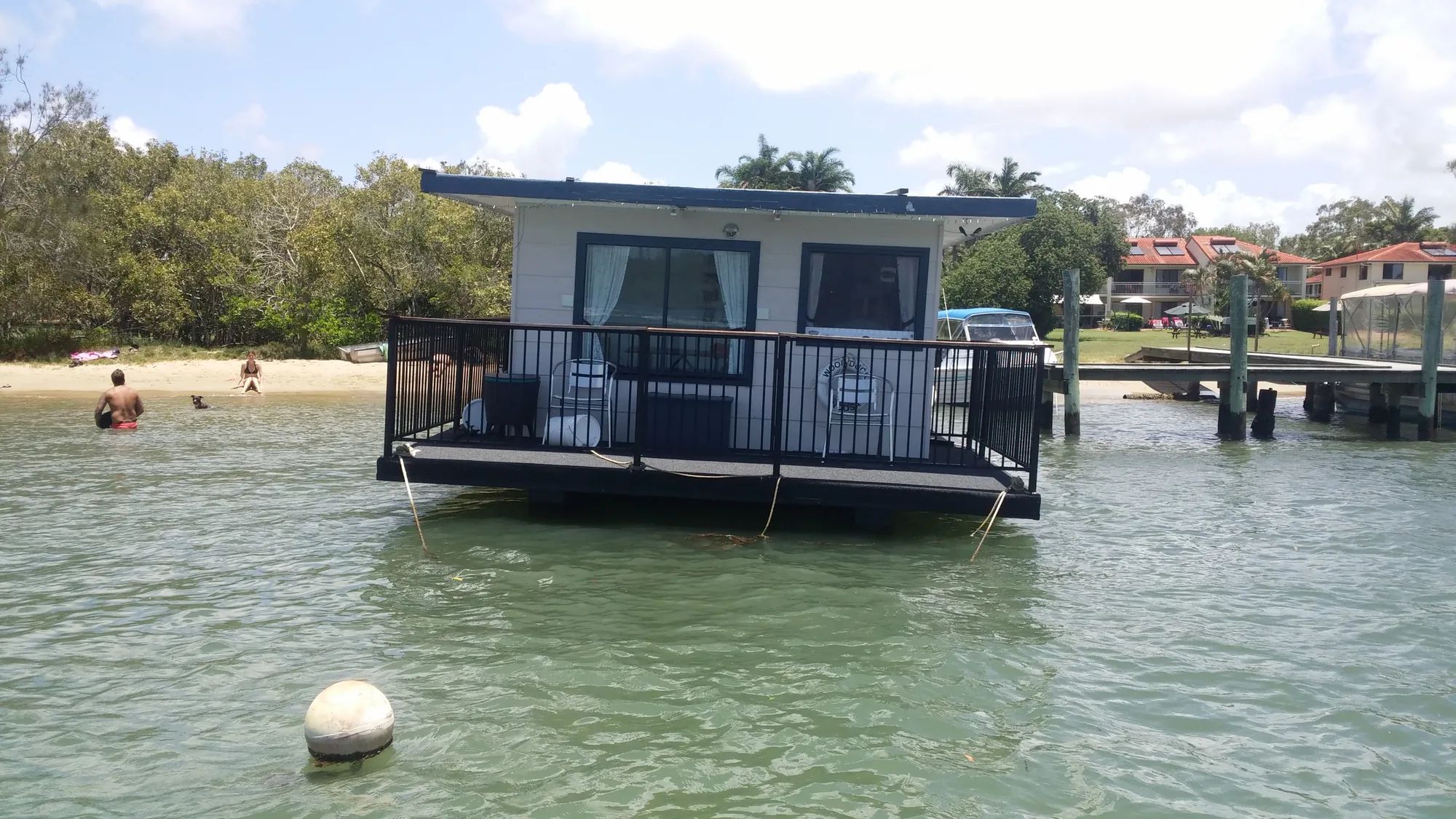 Floating cabin with a railed deck moored off a beach at Noosa