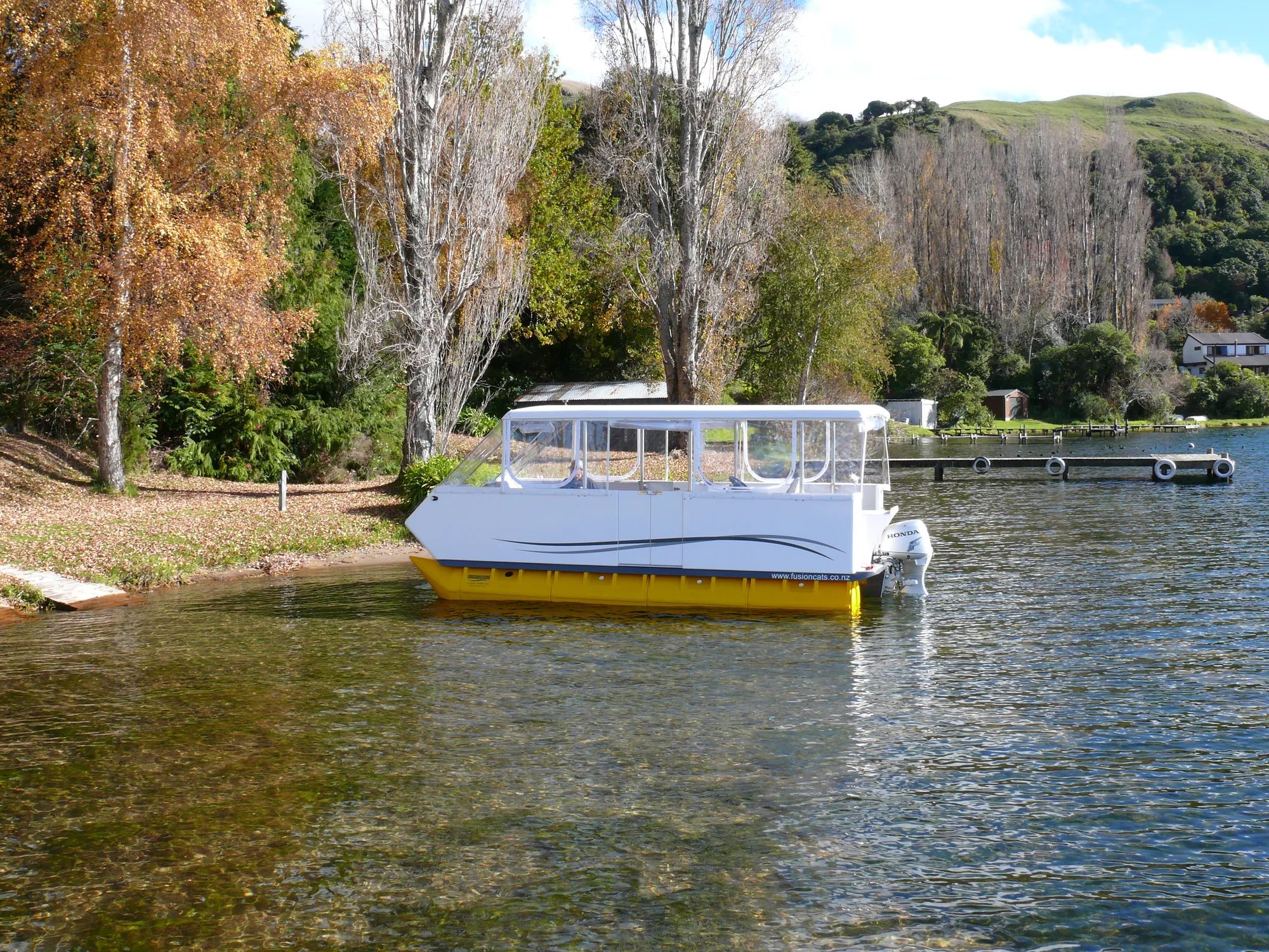Fusion 570 pontoon boat moored at a lakeside with autumn trees