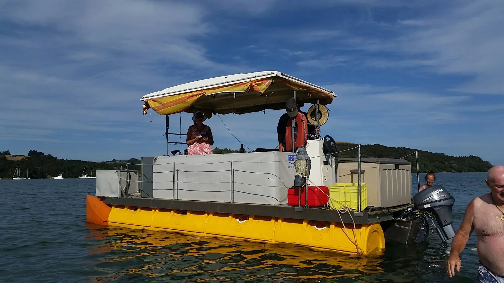 Yellow pontoon boat with a canopy, with a swimmer alongside