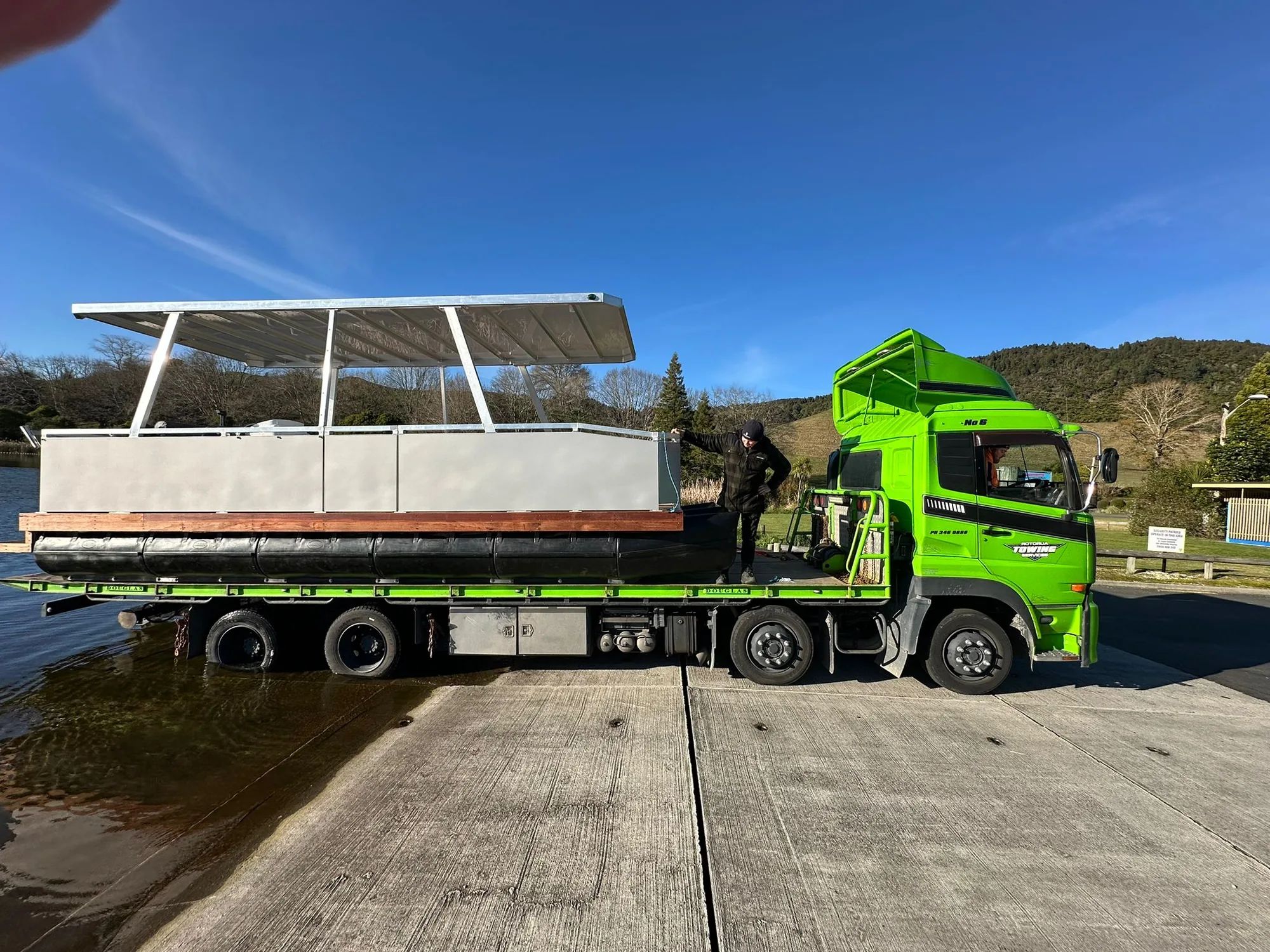 Pontoon boat being delivered on a truck at a boat ramp