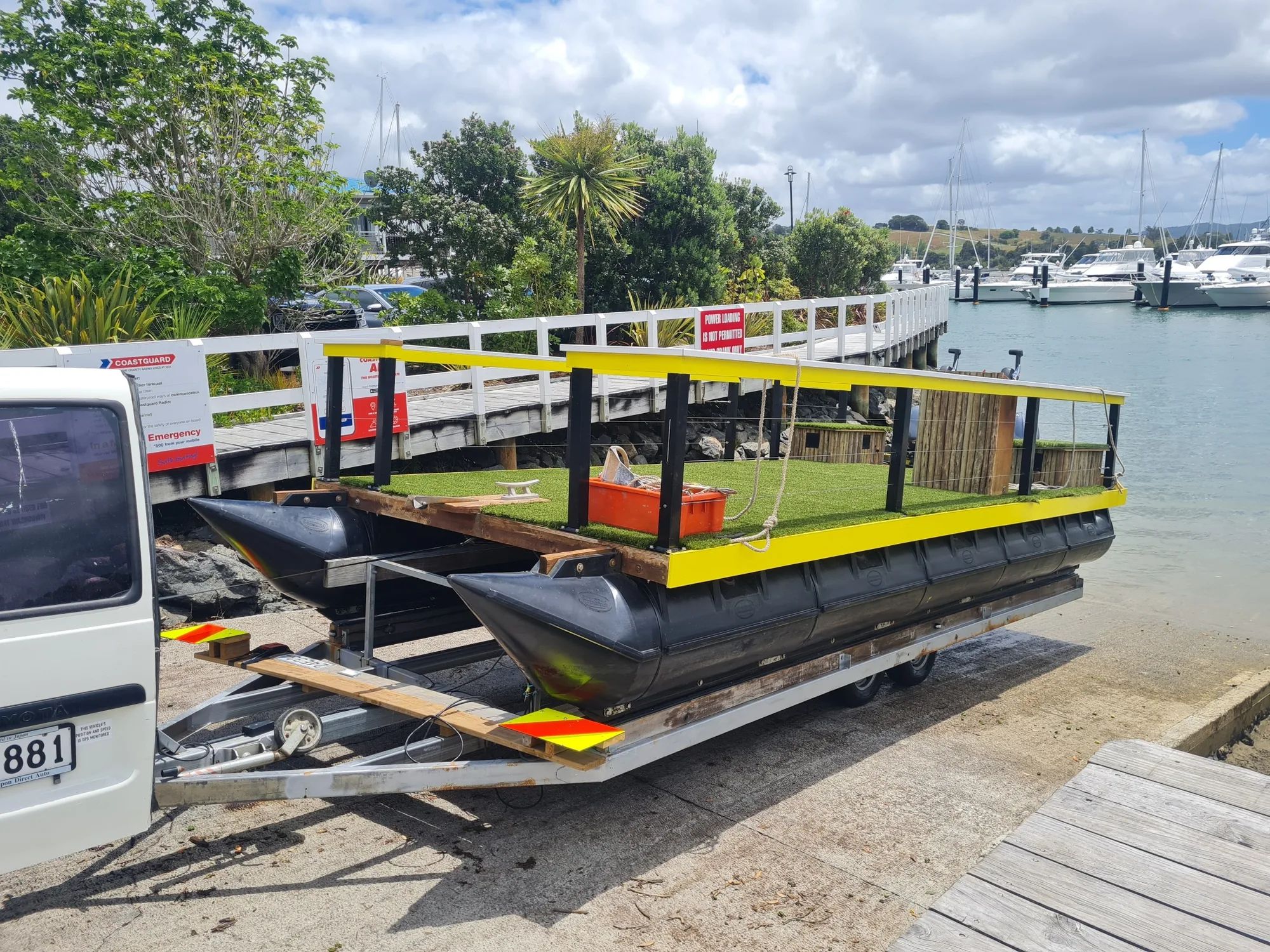 Pontoon boat with a grass-look deck and yellow rails on a trailer at a marina