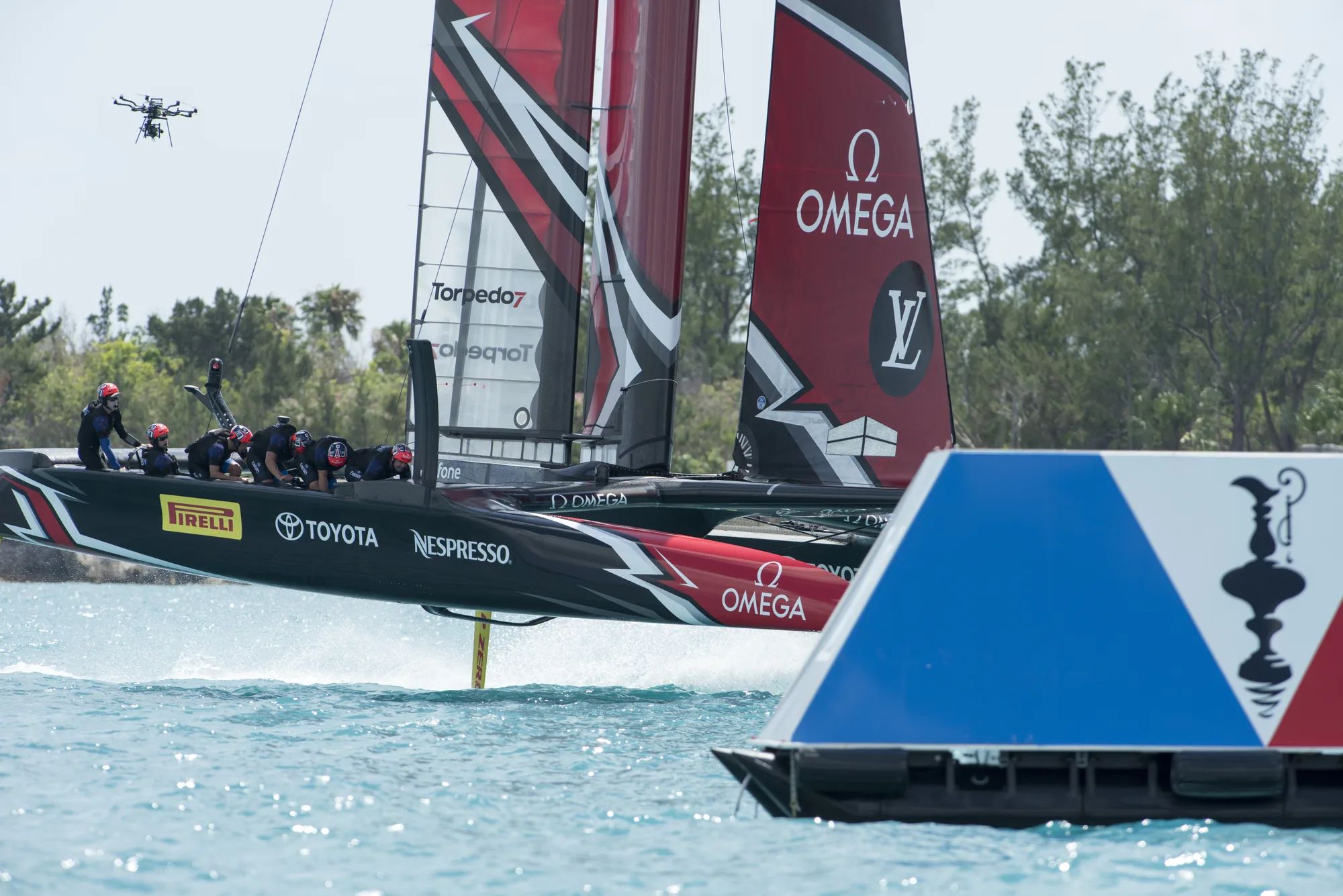 America’s Cup catamaran foiling past a red, white and blue race mark pontoon