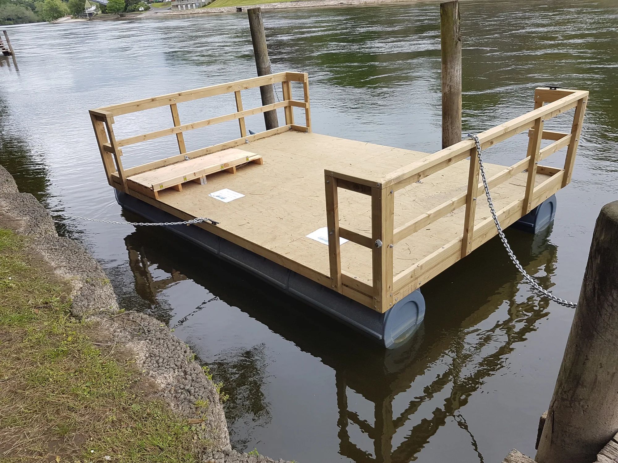 Timber-decked pontoon with rails moored at a riverbank in the Waikato