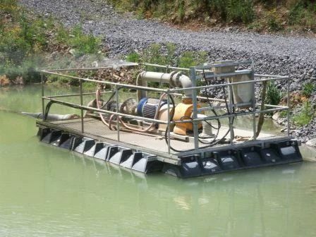 Pump and dredge barge with railings in a muddy settling pond