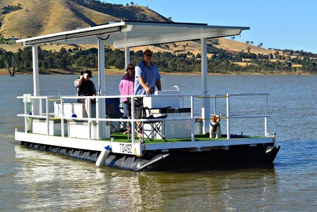 Family and a dog aboard a covered pontoon boat on a lake, hills behind