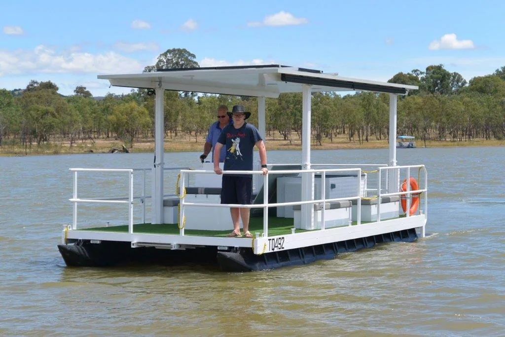 Covered pontoon boat with a solar-panel roof and railings, two people aboard
