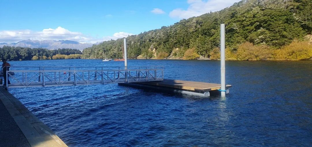 Gangway to a floating timber landing on a lake, mountains behind