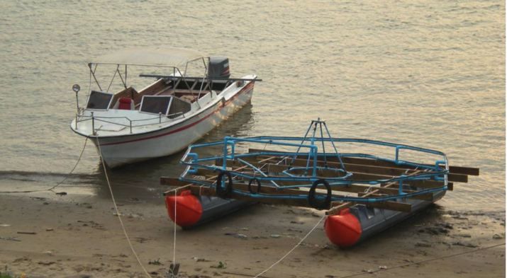 Small mine detector barge on orange pods on a riverbank