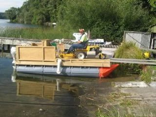 Ride-on mower driving onto a small pod barge