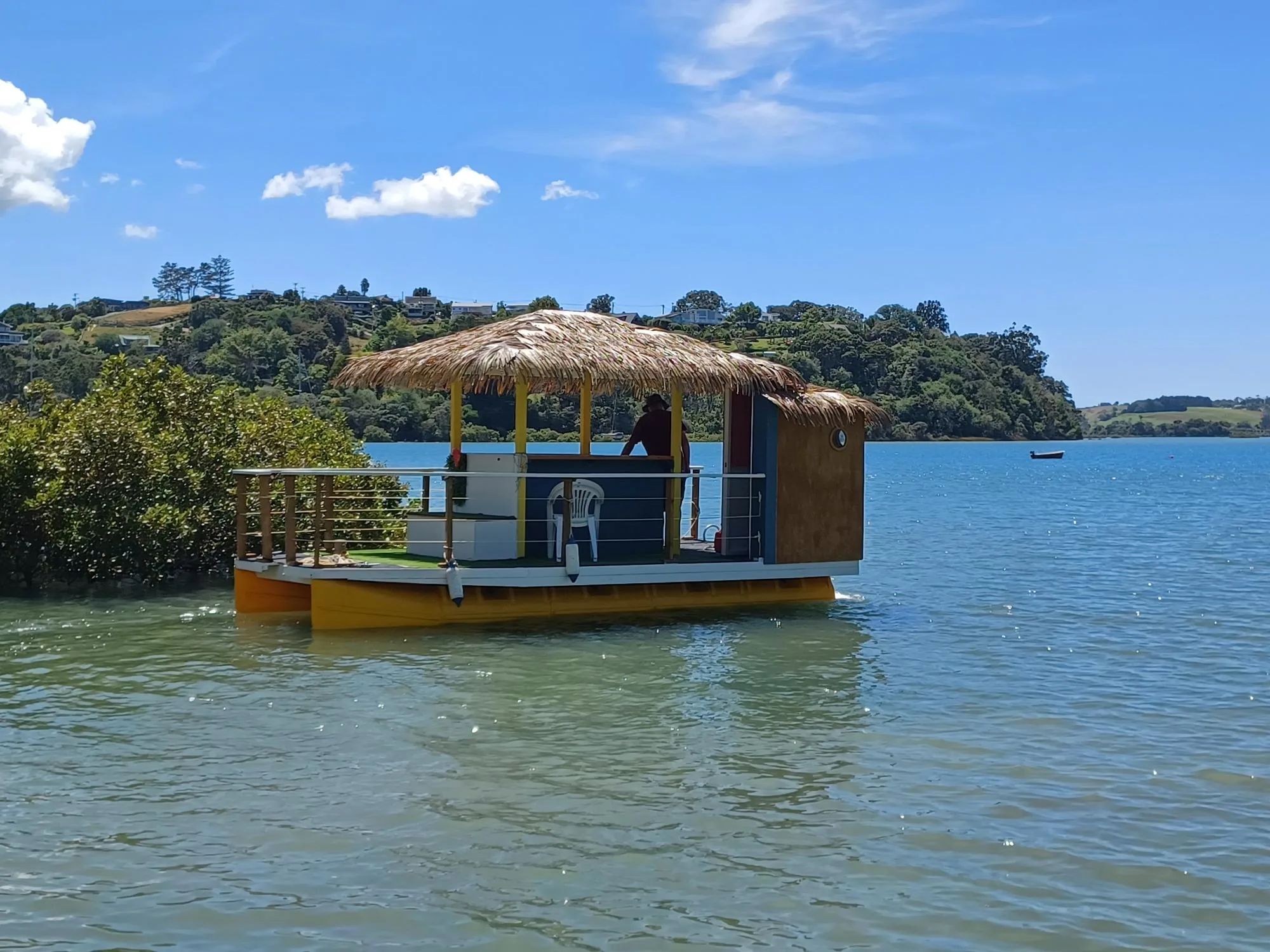 Tiki bar boat with a thatched roof on yellow pods, moored beside mangroves