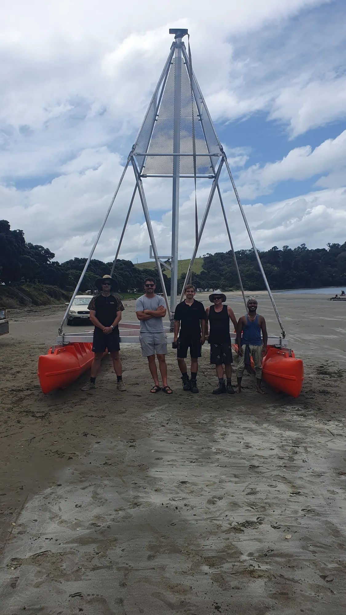 Five people on a beach in front of a tall metal tower frame on orange pods
