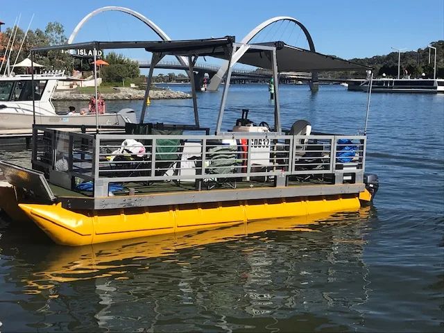 Pontoon boat on yellow pods with a shade roof, moored near an arched footbridge